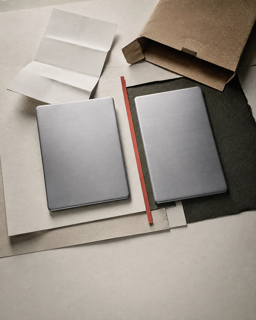 Two unbranded silver devices, blank paper and a kraft package, separated by a vermilion strip.